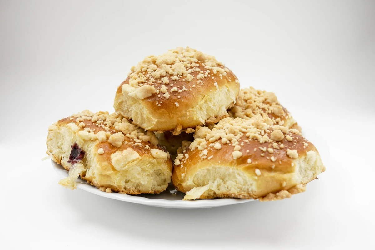 Upieczone jagodzianki z kruszonką ułożone na białym talerzu, widoczne przekrojenie z nadzieniem jagodowym